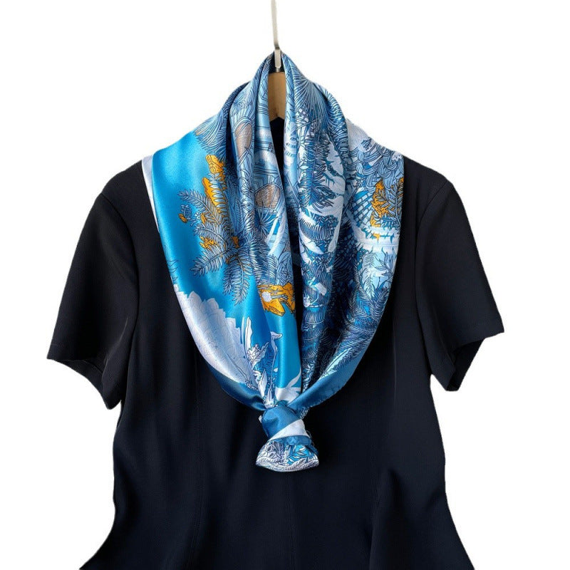 Blue silk square scarf with tropical leaf and bird print, tied on a black top.