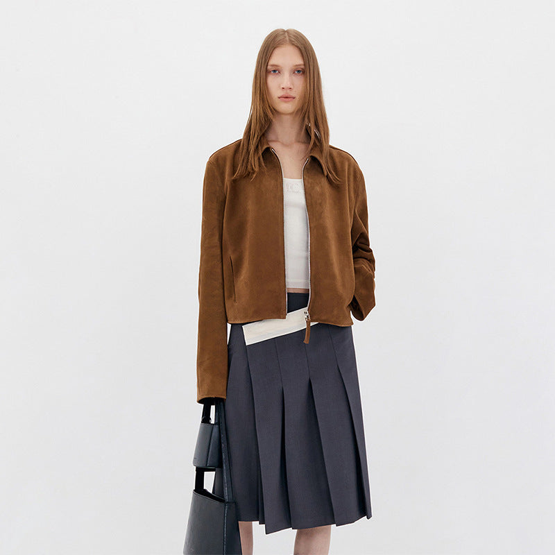 Brown cropped suede jacket with a front zipper, modeled with a pleated skirt.
