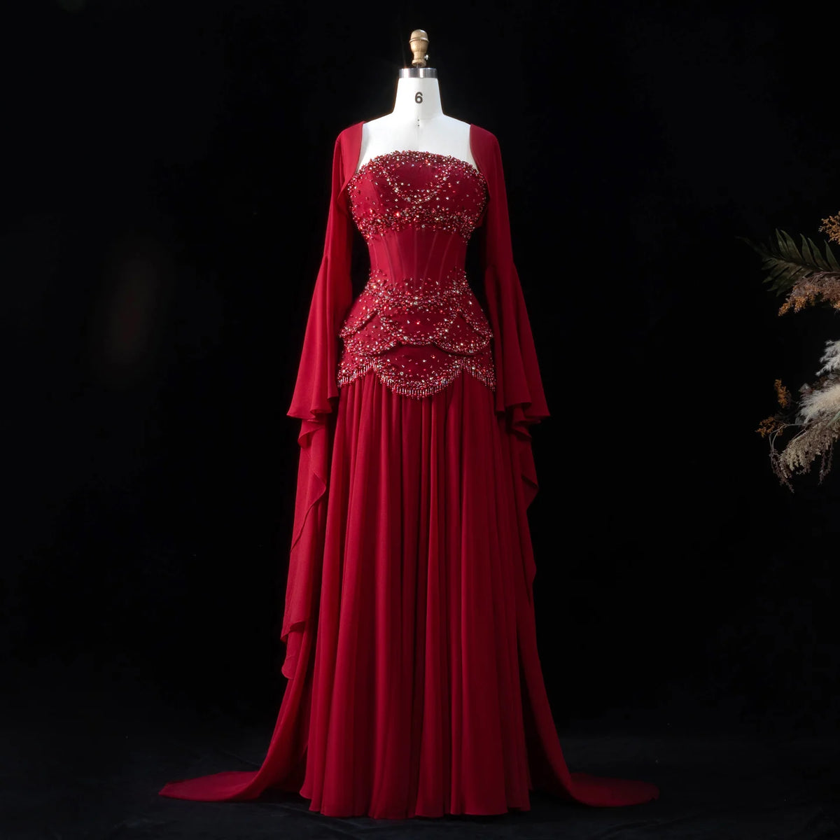 Red beaded corset evening gown with a flowing skirt and long flared sleeves
