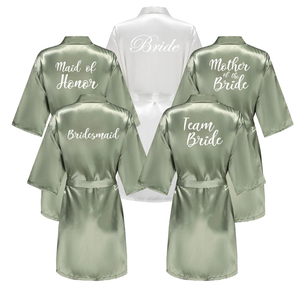 Five satin wedding robes in white and sage green with bridal party titles on the backs