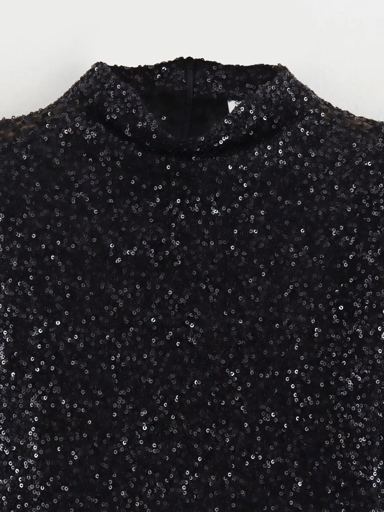 Black sequin dress fabric close-up with round neckline and textured sequins
