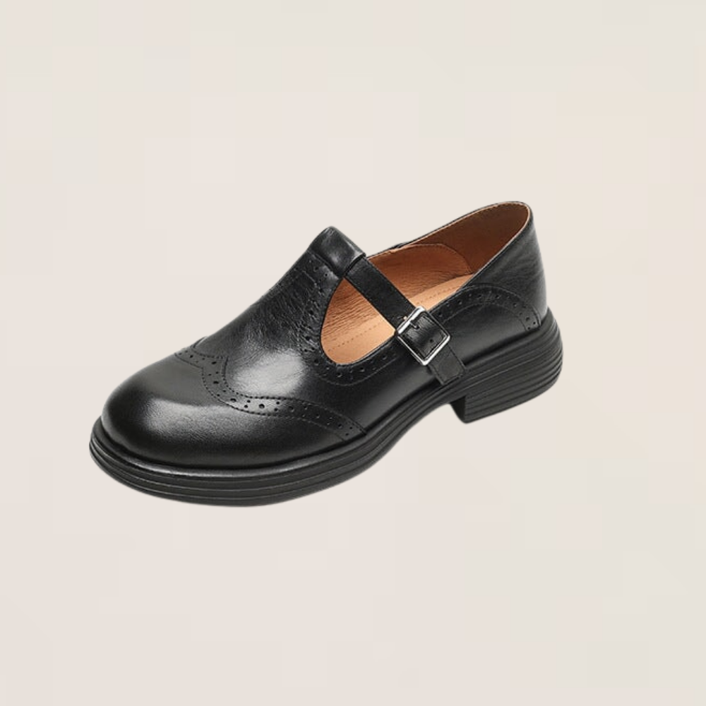 Black leather Mary Jane flat with T-strap buckle, brogue perforations, and low block heel.